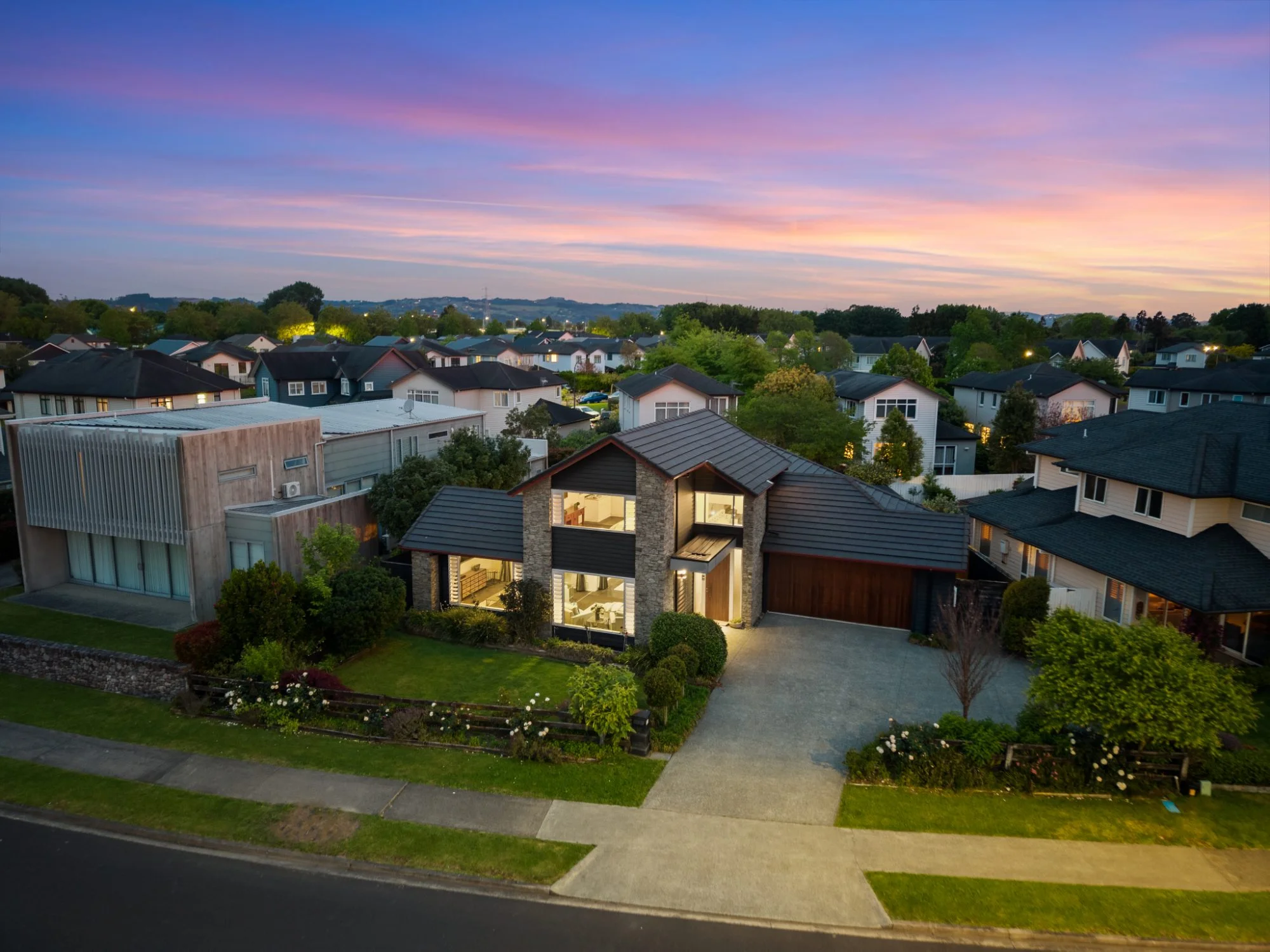 Twilight drone photo of a two-storey home in Karaka with the interior lit